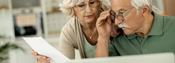 Eine ältere Dame und ein älterer Herr betrachten ein Schriftstück.