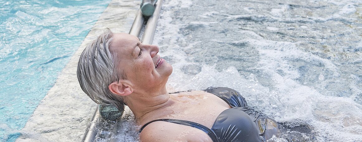 Senior white woman enjoying water massage. Hydromassage in outdoor thermal swimming pool.