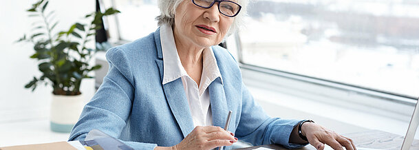 Attractive serious female chief executive officer of mature age sitting at her office with laptop, keyboarding and signing papers on desk, having confident look. People, aging, job and career concept