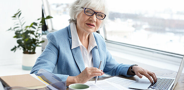Attractive serious female chief executive officer of mature age sitting at her office with laptop, keyboarding and signing papers on desk, having confident look. People, aging, job and career concept Attractive serious female chief executive officer of mature age sitting at her office with laptop, keyboarding and signing papers on desk, having confident look. People, aging, job and career concept