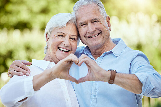 Shot of a senior couple forming a heart shape with their hands while standing outside