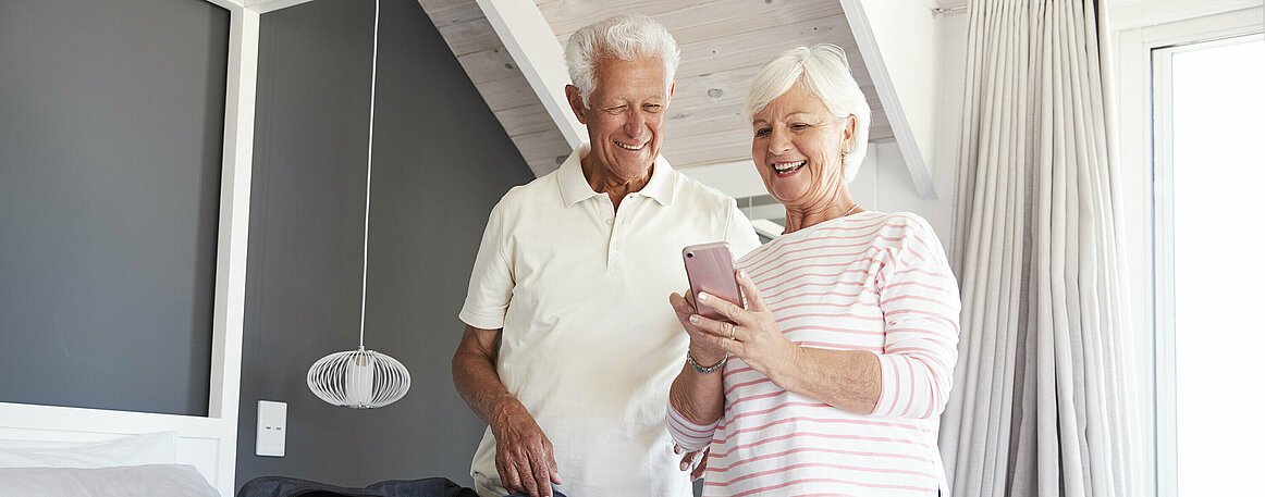 Senior Couple Look At Mobile As They Check In To Vacation Rental