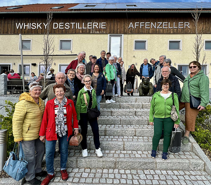 Pensionist/Innen stehen auf Treppe vor Haus der Whisky-Destillerie