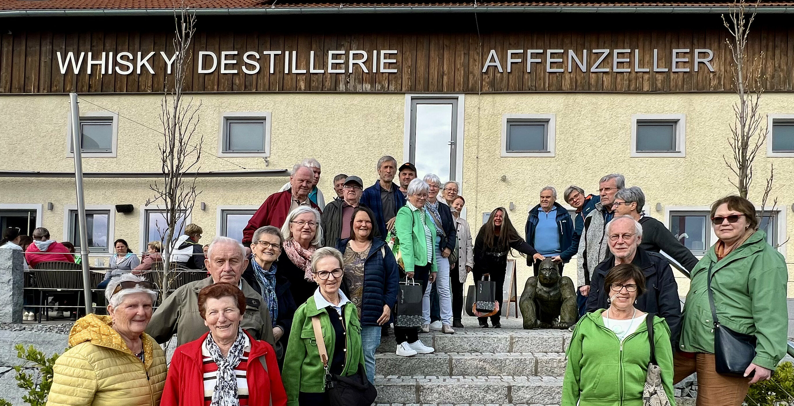 Pensionist/Innen stehen auf Treppe vor Haus der Whisky-Destillerie