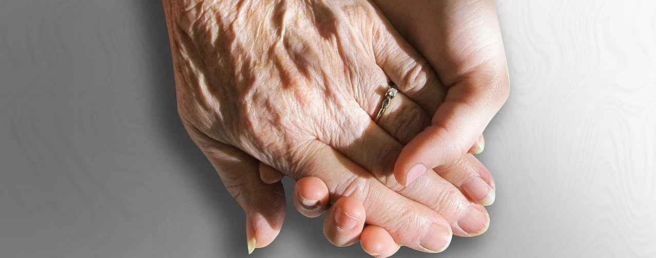 Hände einer älteren Person mit Ring und einer jüngeren Person auf grauem Hintergrund