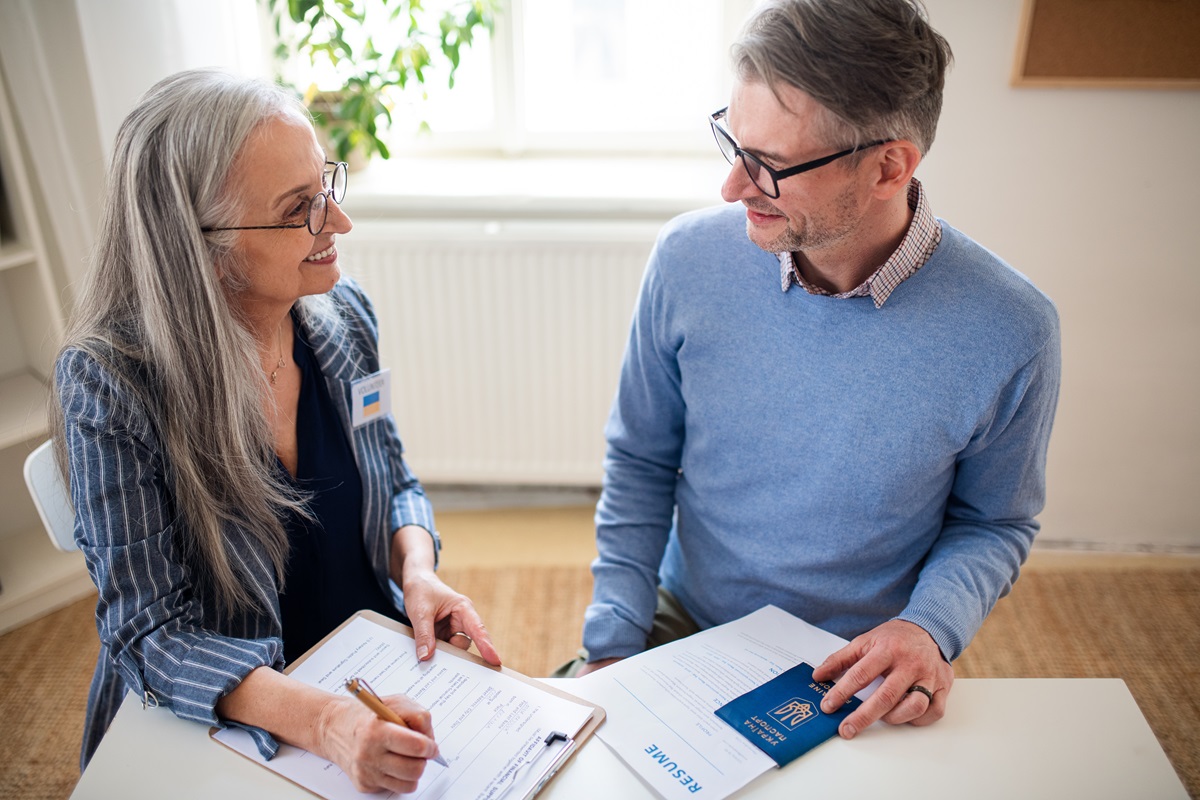GEsetzliche Änderung ab 1.1.2026 Senior woman volunteer helping Ukrainian man to fill in forms at asylum centre.